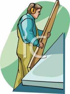 A worker wearing ear protection and overalls carries a wooden plank while standing on a platform.