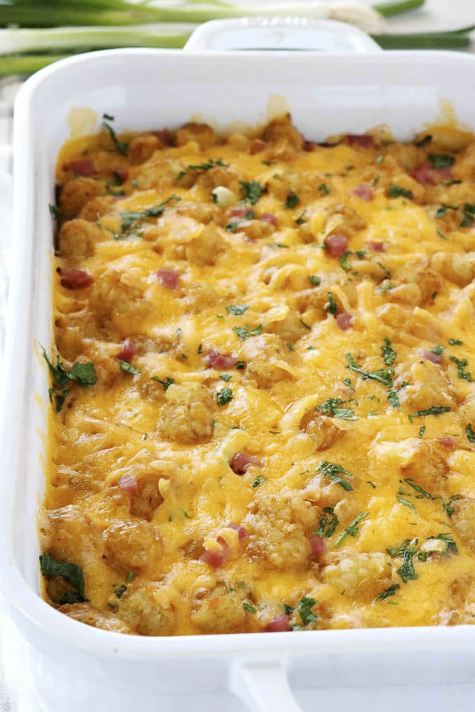 Cheesy tater tot casserole with ham and herbs in a white baking dish, garnished with fresh parsley.