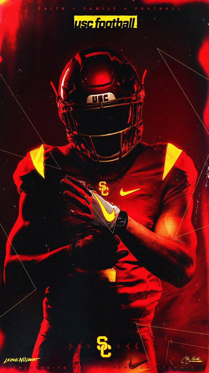 USC football player in black and gold uniform with red lighting, holding a football, helmet visor down.