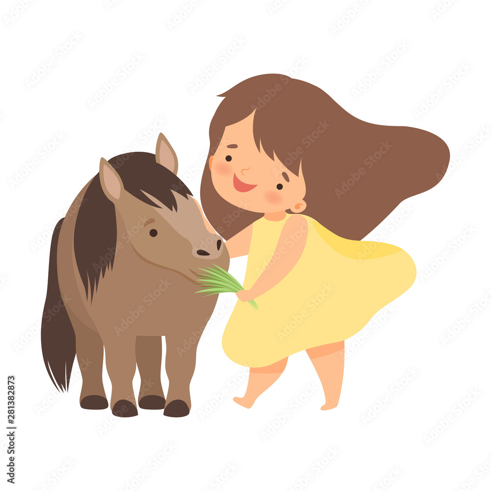 Smiling girl in yellow dress feeding grass to a small brown pony.