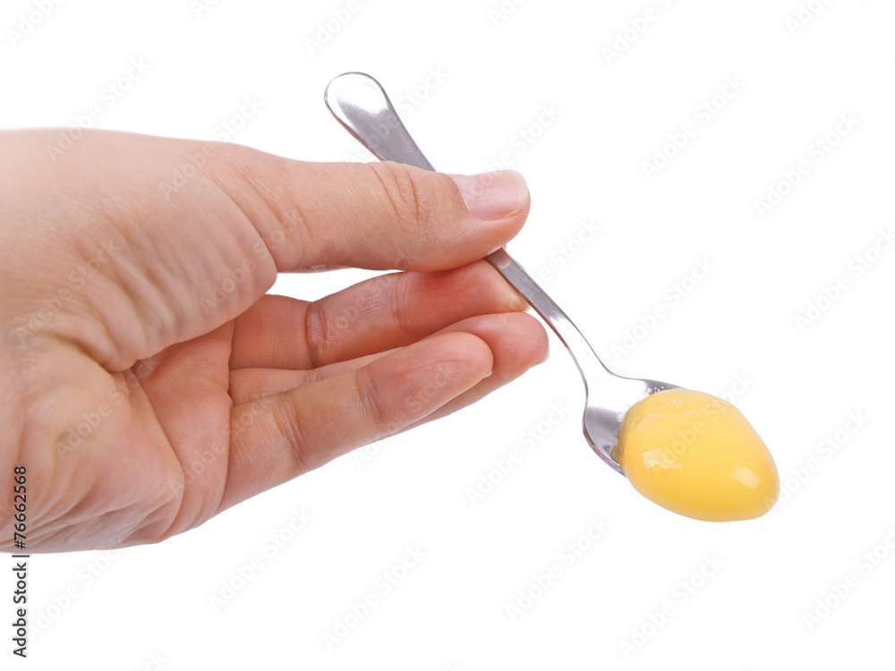 Hand holding a spoon with raw egg yolk against white background