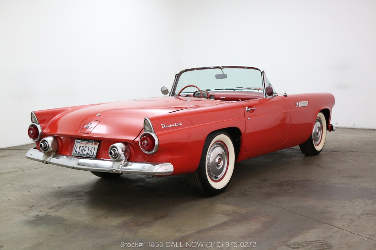 Classic 1955 Ford Thunderbird convertible in vibrant red with white-wall tires and chrome details, rear three-quarter view.