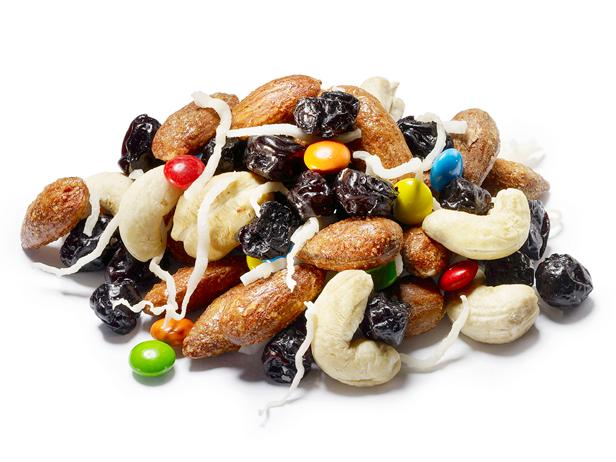 Trail mix with almonds, cashews, raisins, colorful candies, and coconut shreds on white background.