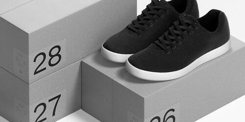 Black minimalist sneakers on numbered gray boxes in monochrome studio shot.