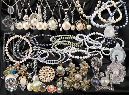 A luxurious collection of vintage and modern pearl jewelry including necklaces, bracelets, earrings, and brooches displayed on black fabric.