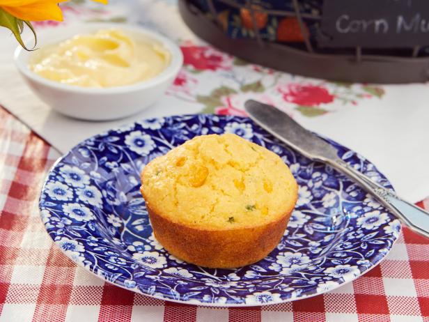 Golden corn muffin on blue floral plate with butter bowl and checkered tablecloth.