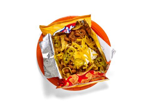 Opened Doritos Nacho Cheese bag filled with nacho toppings-jalapeños, cheese, sour cream, and ground beef-on an orange plate.