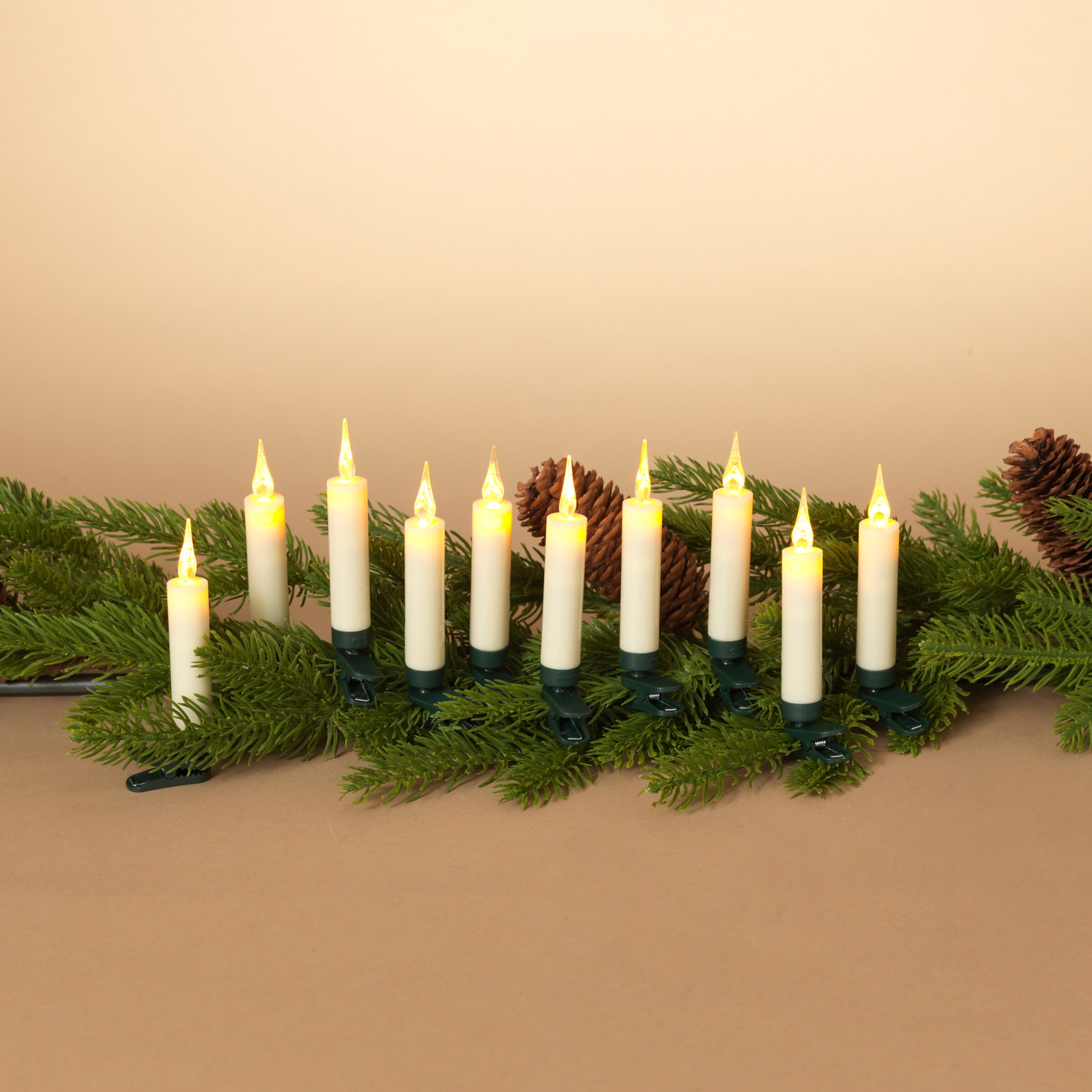 LED candle lights clipped onto green garland with pinecones, warm white glow against beige background.
