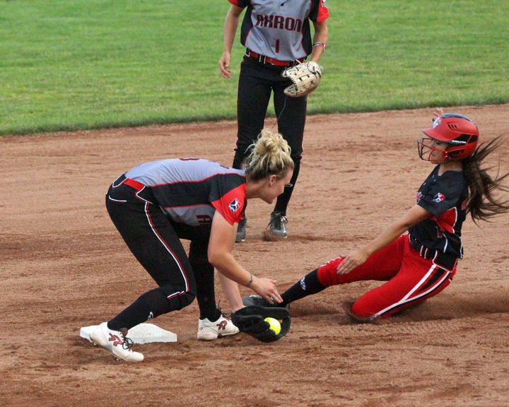 A softball player in red slides into second base as the defender tags her out with a glove and yellow ball.