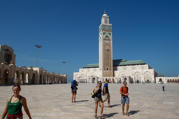 Hassan II Mosque in Casablanca, Morocco, with visitors in the expansive courtyard under a clear blue sky.