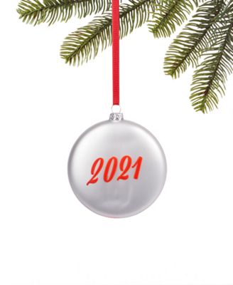 Silver Christmas ornament with "2021" in red script, hanging from a pine branch by a red ribbon.
