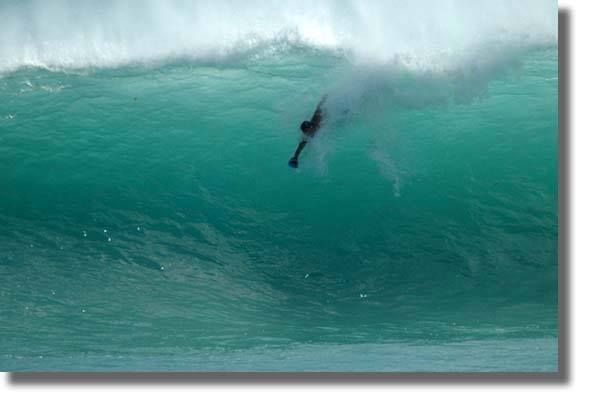 Surfer mid-air inside a massive turquoise barrel wave, water spraying as the lip curls overhead.