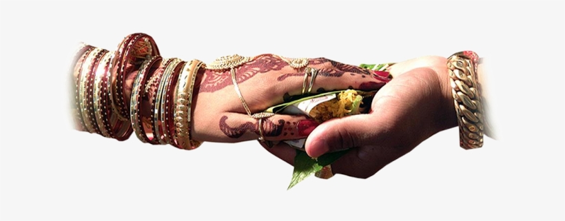 A bride's henna-adorned hand holding a ceremonial leaf with turmeric and rice, adorned with bangles and rings.