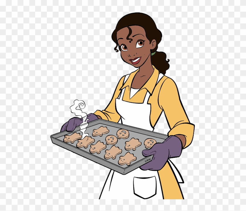 A smiling Black woman in a yellow shirt and white apron holds a baking tray of steaming animal-shaped cookies.