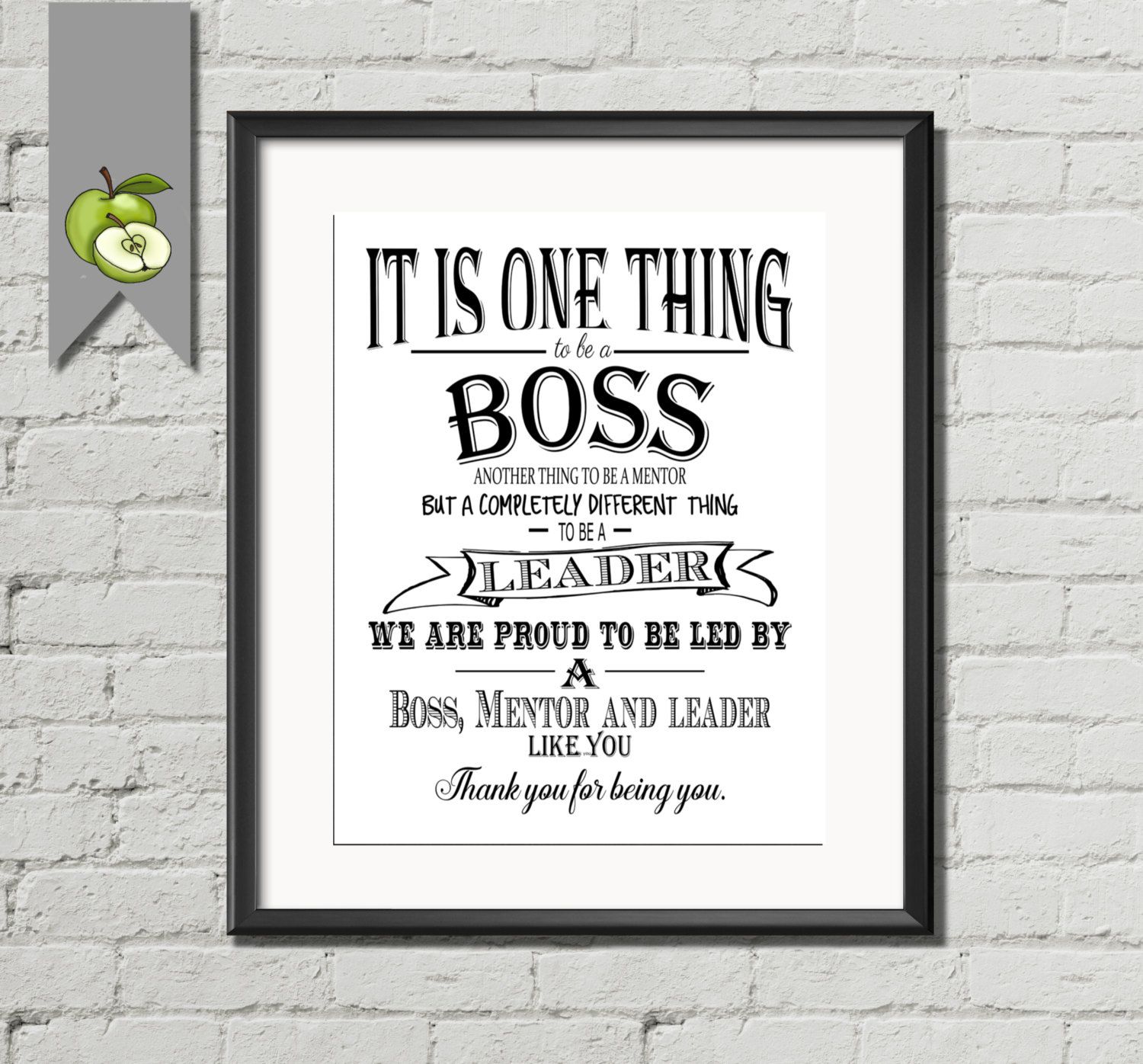 Framed inspirational print distinguishing boss, mentor, and leader roles, mounted on white brick wall with green apple banner.