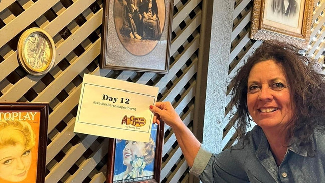 A smiling woman holds up a "Day 12" sign with vintage theater posters in the background.