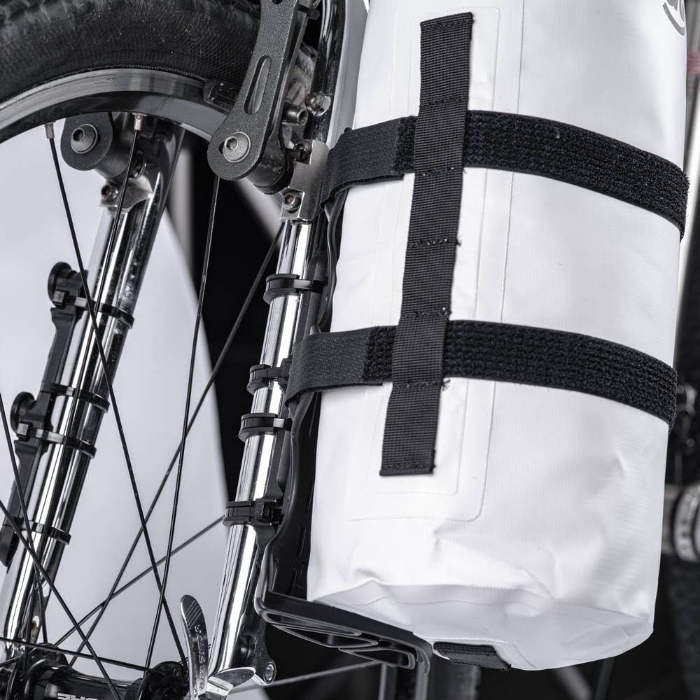 White waterproof bikepacking frame bag secured with black straps to a bicycle fork and front wheel.