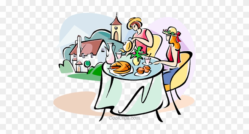 Two women enjoying tea and pastries at a table with a quaint village in the background.