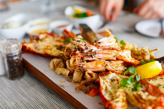 Fresh seafood platter featuring lobster, prawns, calamari, lemon, and herbs on a wooden board with condiments nearby.