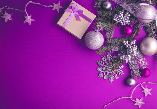 Purple holiday flat lay with gift box, silver and magenta ornaments, pine branches, star lights, and snowflake decor.