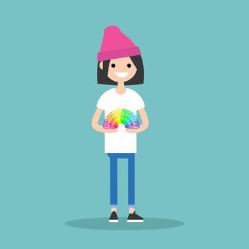 Young woman in pink beanie holding a rainbow-colored slinky toy, smiling against teal background.