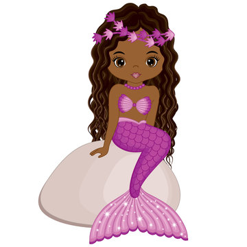 A smiling dark-skinned mermaid with long curly brown hair, pink flower crown, and shimmering pink tail sitting on a rock.