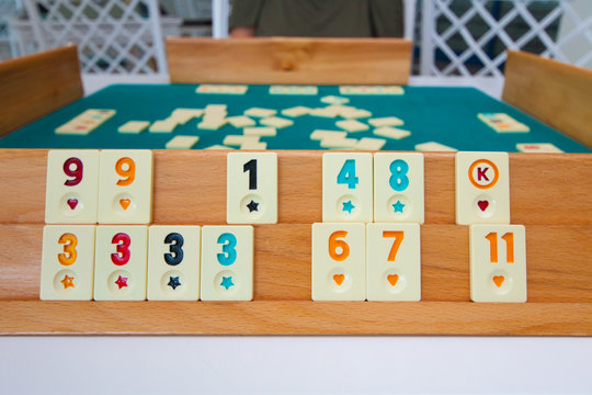 Rummikub tile game setup with numbered and joker tiles arranged on a wooden rack over a green felt table.
