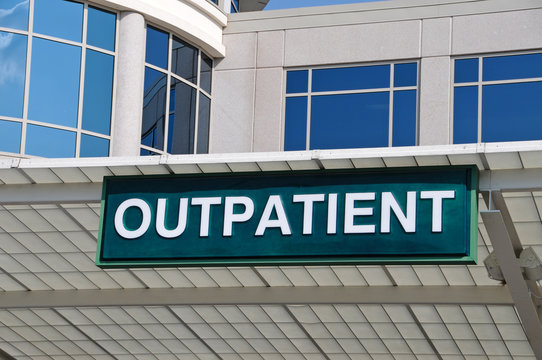 Green "OUTPATIENT" sign mounted on a modern medical building facade with reflective windows.