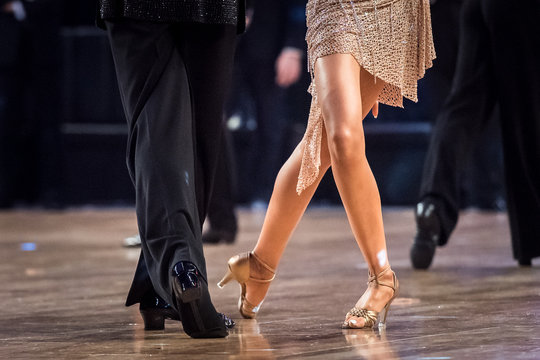 Close-up of ballroom dancers' legs and feet mid-step on a polished dance floor, wearing elegant shoes and formal attire.