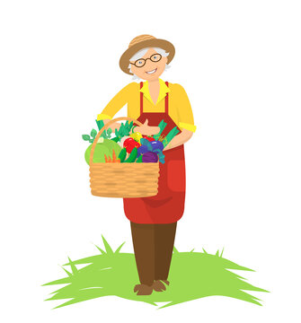 Smiling elderly woman in apron and hat holding a basket of fresh vegetables on grass.