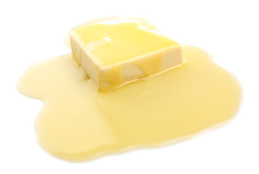 A pat of pale yellow butter melting into a glossy pool on a white surface.