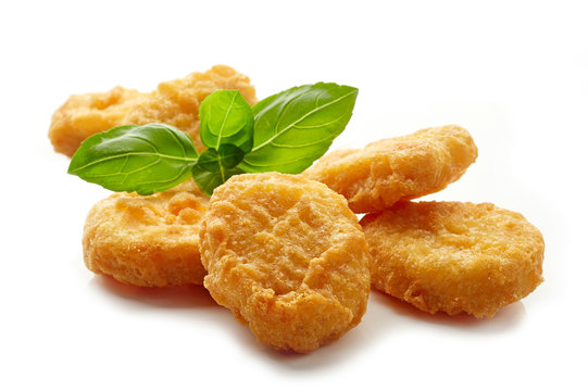 Crispy golden chicken nuggets garnished with fresh basil leaves on a white background.