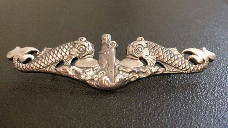 Silver naval insignia featuring two stylized fish flanking a central tower, symbolizing maritime service and tradition.