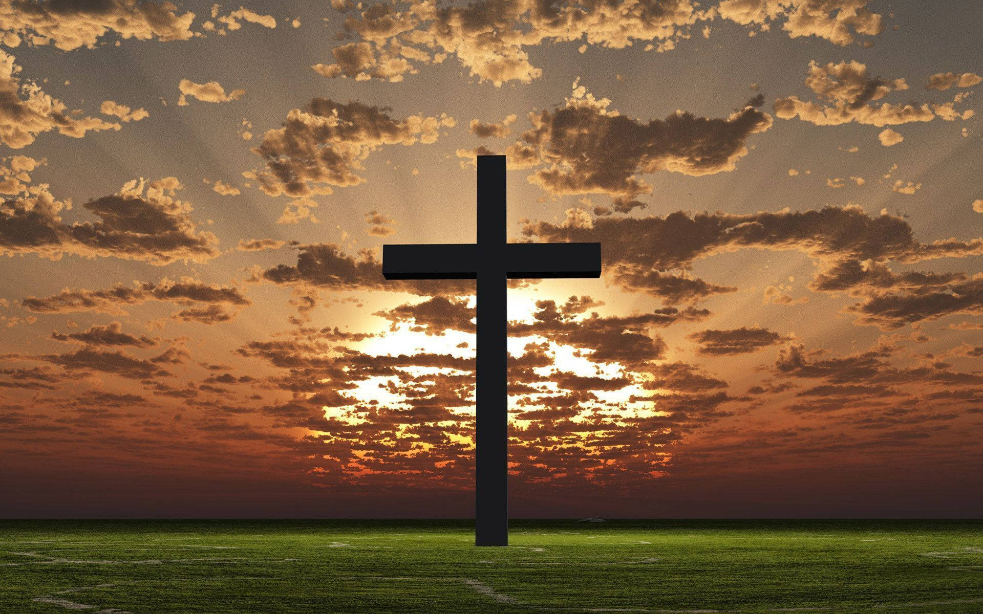 Silhouetted Christian cross standing in a green field at sunset with golden clouds and sun rays breaking through.