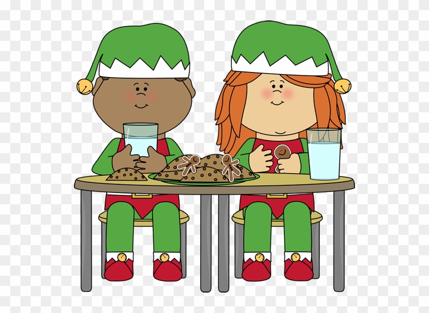 Two cheerful elves in green and red outfits sit at a table eating cookies and drinking milk.
