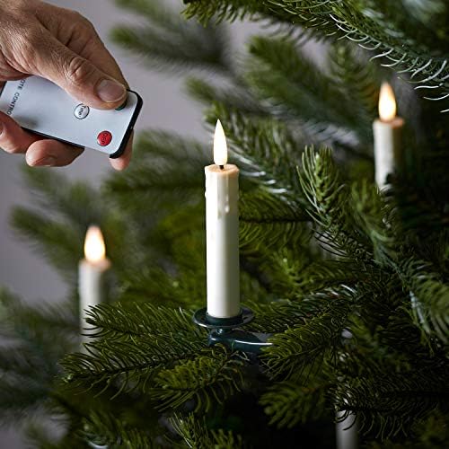 Hand holding remote control turning on flameless LED candles on a Christmas tree branch.