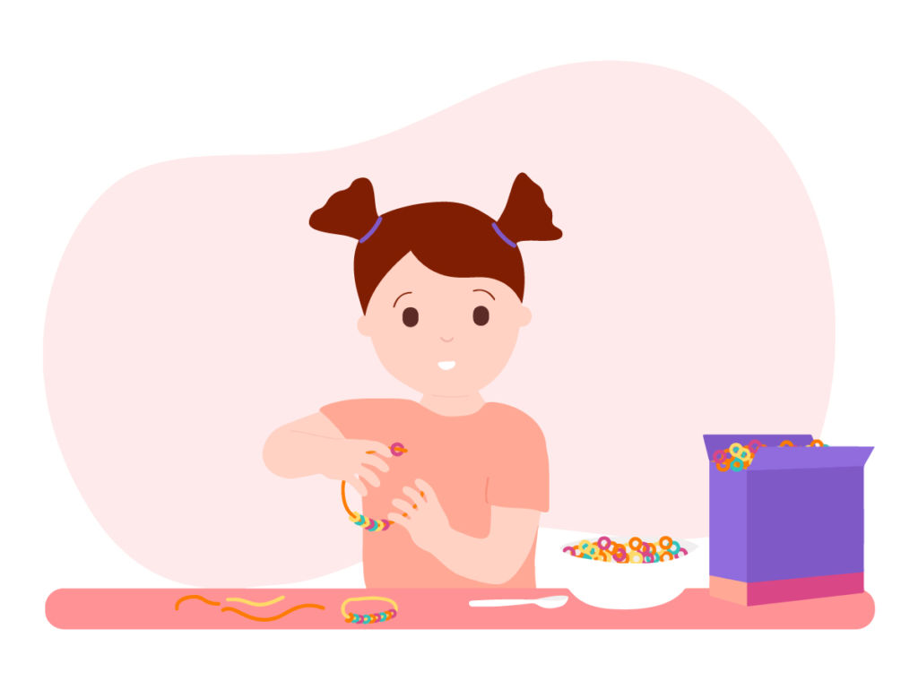 A young girl with pigtails makes a colorful beaded bracelet at a table with cereal and craft supplies.