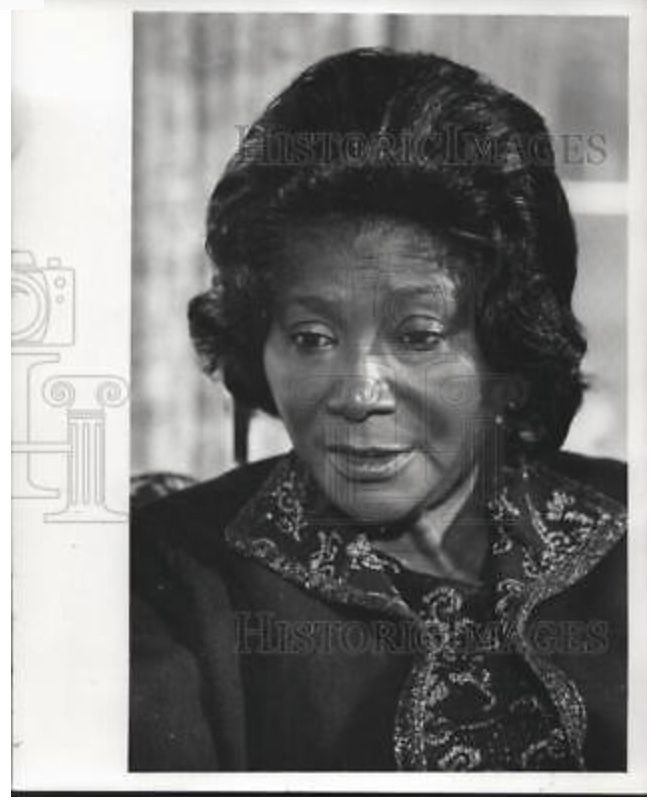 Black-and-white portrait of a mature Black woman with styled hair and ornate collar, looking thoughtfully toward the camera.