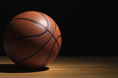 A classic orange basketball with black seams rests on a wooden court under dramatic lighting against a black background.