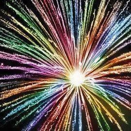 Vibrant multicolored light burst radiating from a bright central point against black background, resembling fireworks or cosmic explosion.