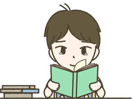A young boy with brown hair reads a green book at a desk, with a stack of books beside him.