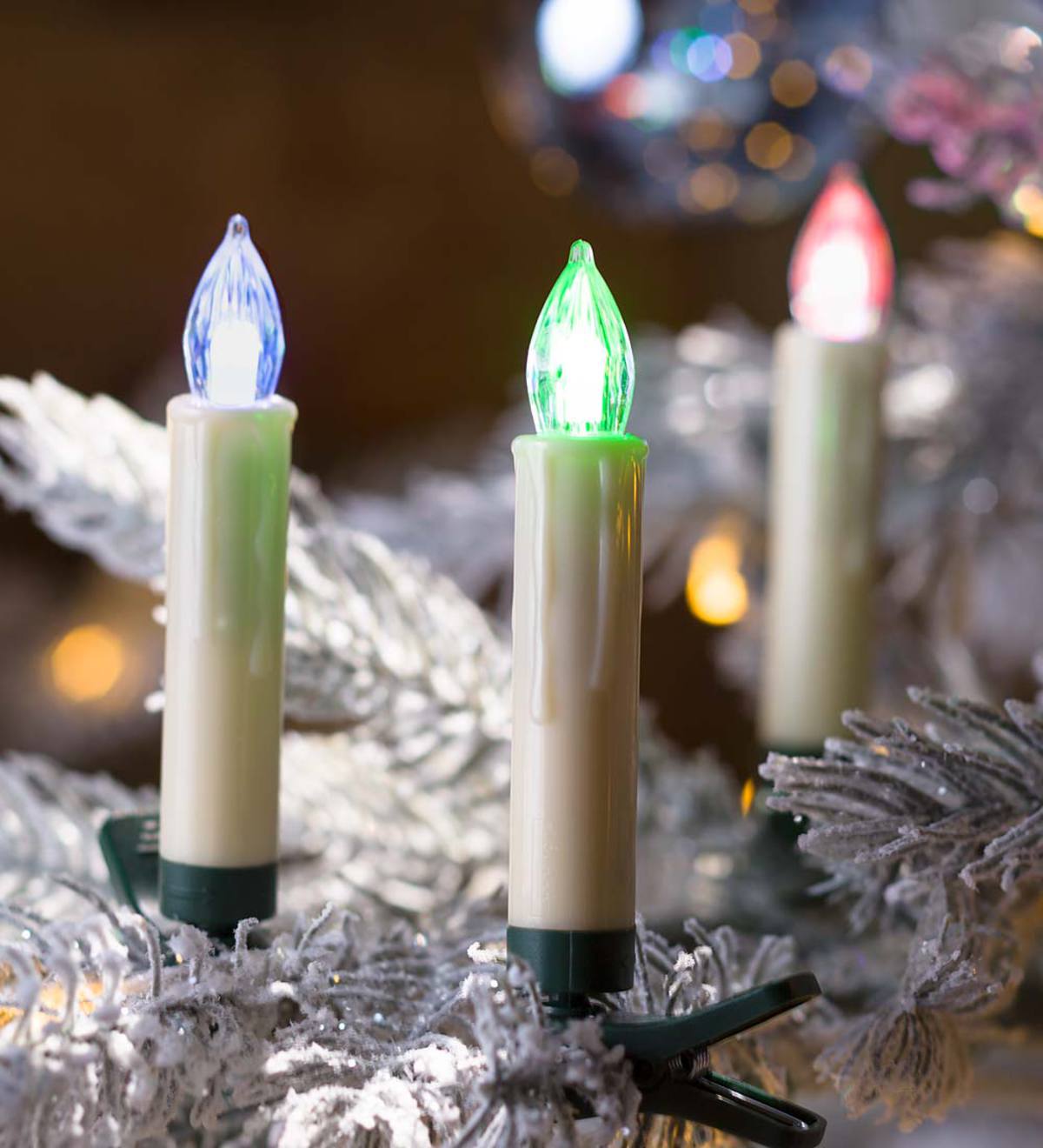 Three LED candle-style Christmas lights in blue, green, and red on a frosted white tree branch.