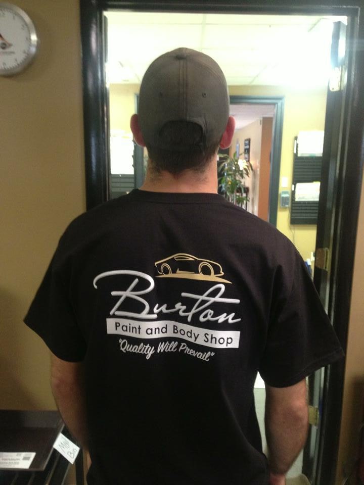Man wearing black Burton Paint and Body Shop t-shirt with logo on back, viewed from behind in office doorway.