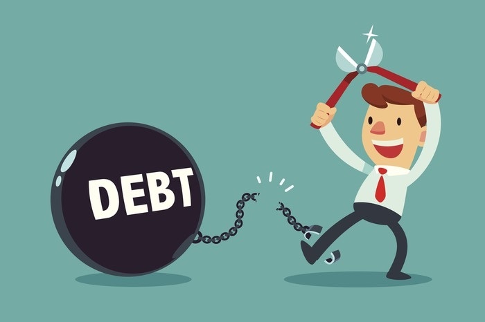 Businessman joyfully cutting chain linking him to a heavy "DEBT" ball with oversized scissors.