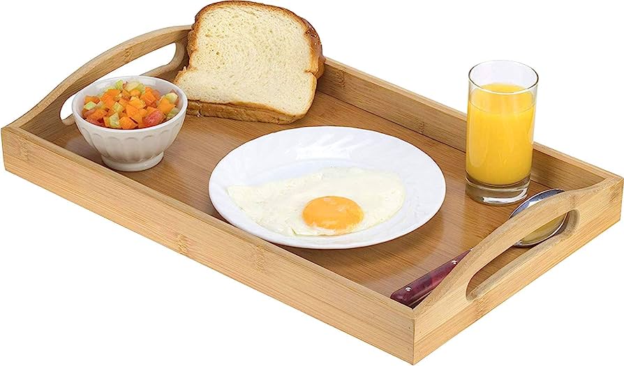 Bamboo breakfast tray with fried egg, toast, fruit salad, orange juice, and cutlery.