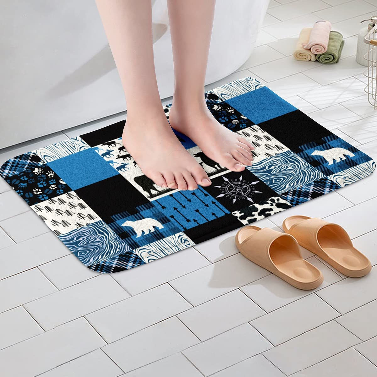 Blue and black patchwork bath mat with bear, paw print, and forest motifs under bare feet in a tiled bathroom.