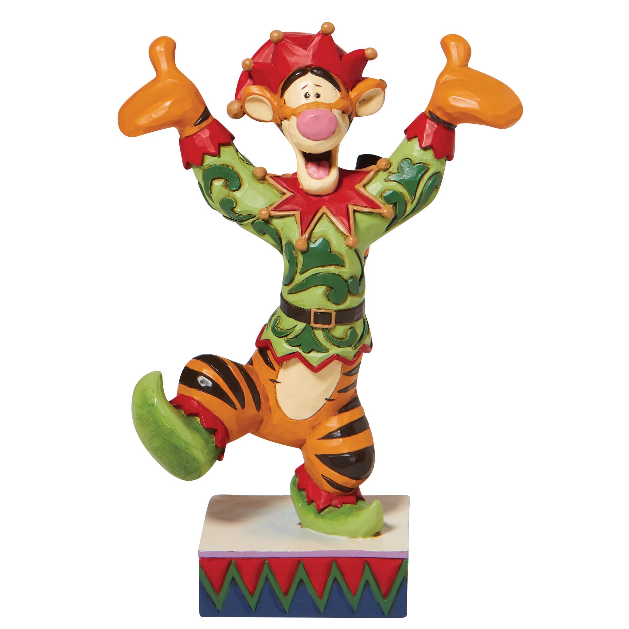 Tigger in festive jester costume with red hat, green tunic, and raised arms giving thumbs-up on decorative base.