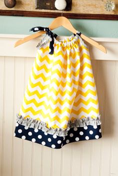Handmade yellow chevron halter dress with navy polka-dot ruffle and black ribbon tie, hanging on wooden hanger.