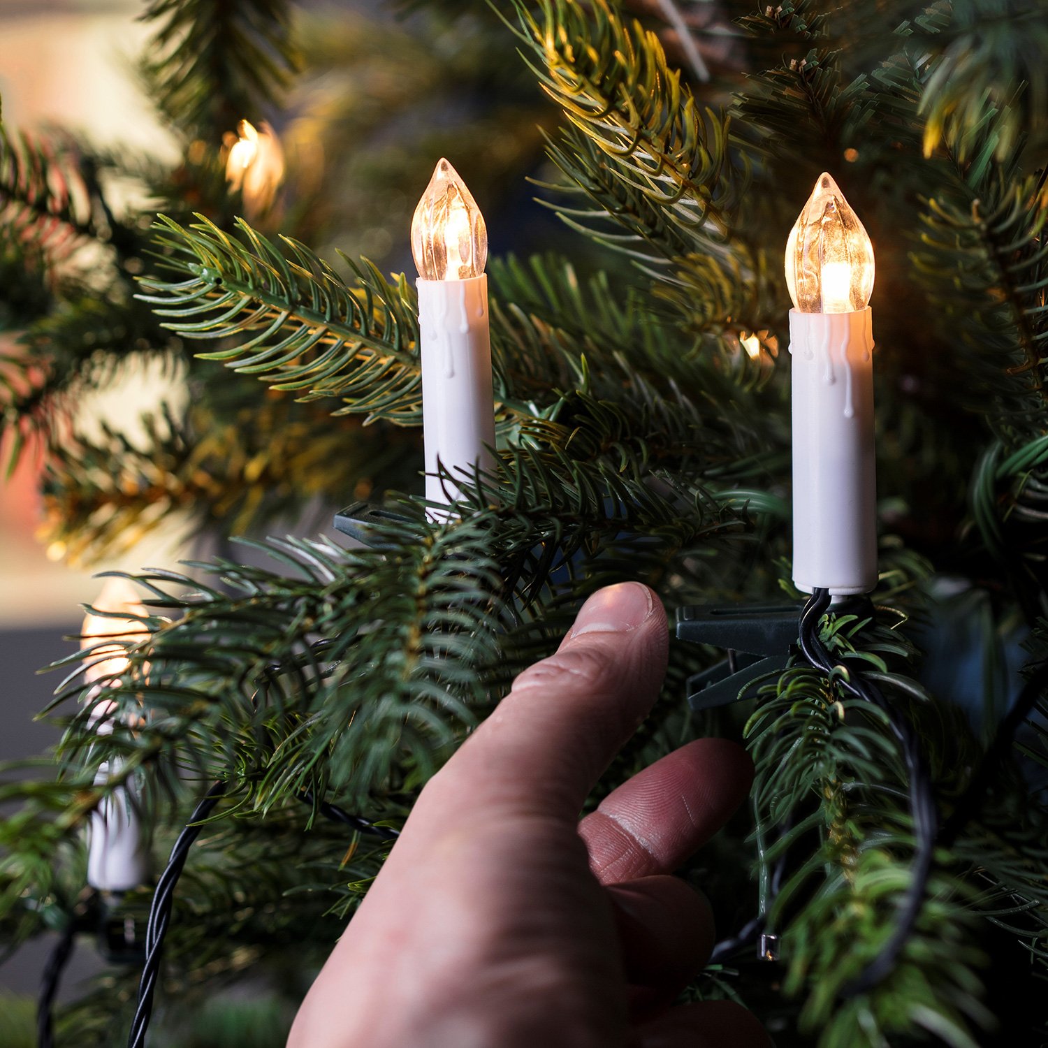 Hand adjusting warm-white candle-style LED Christmas lights on a pine tree branch.