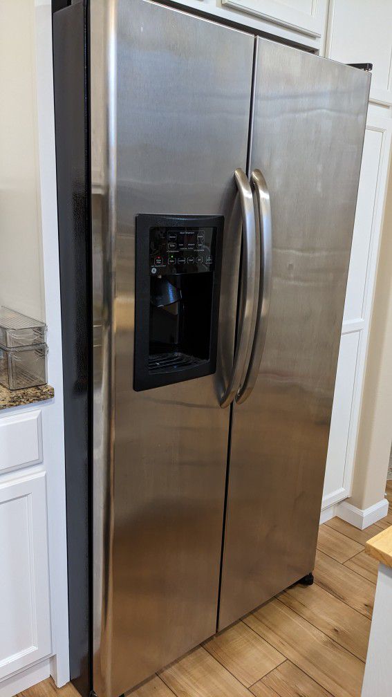 Stainless steel side-by-side refrigerator with water and ice dispenser in modern kitchen setting.